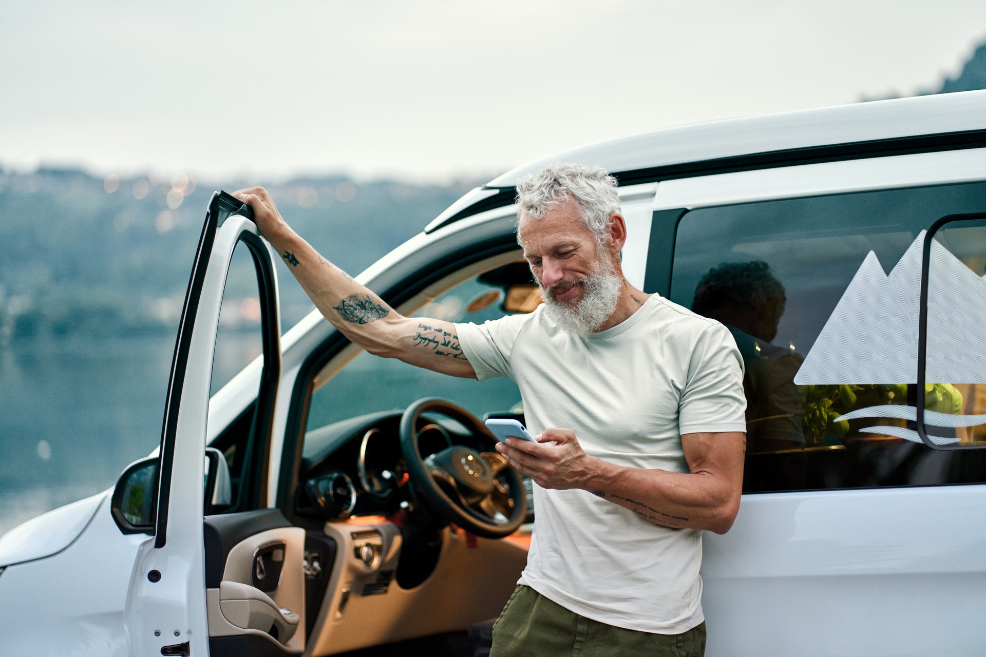 Mature man traveler standing near camper van using mobile in camping.