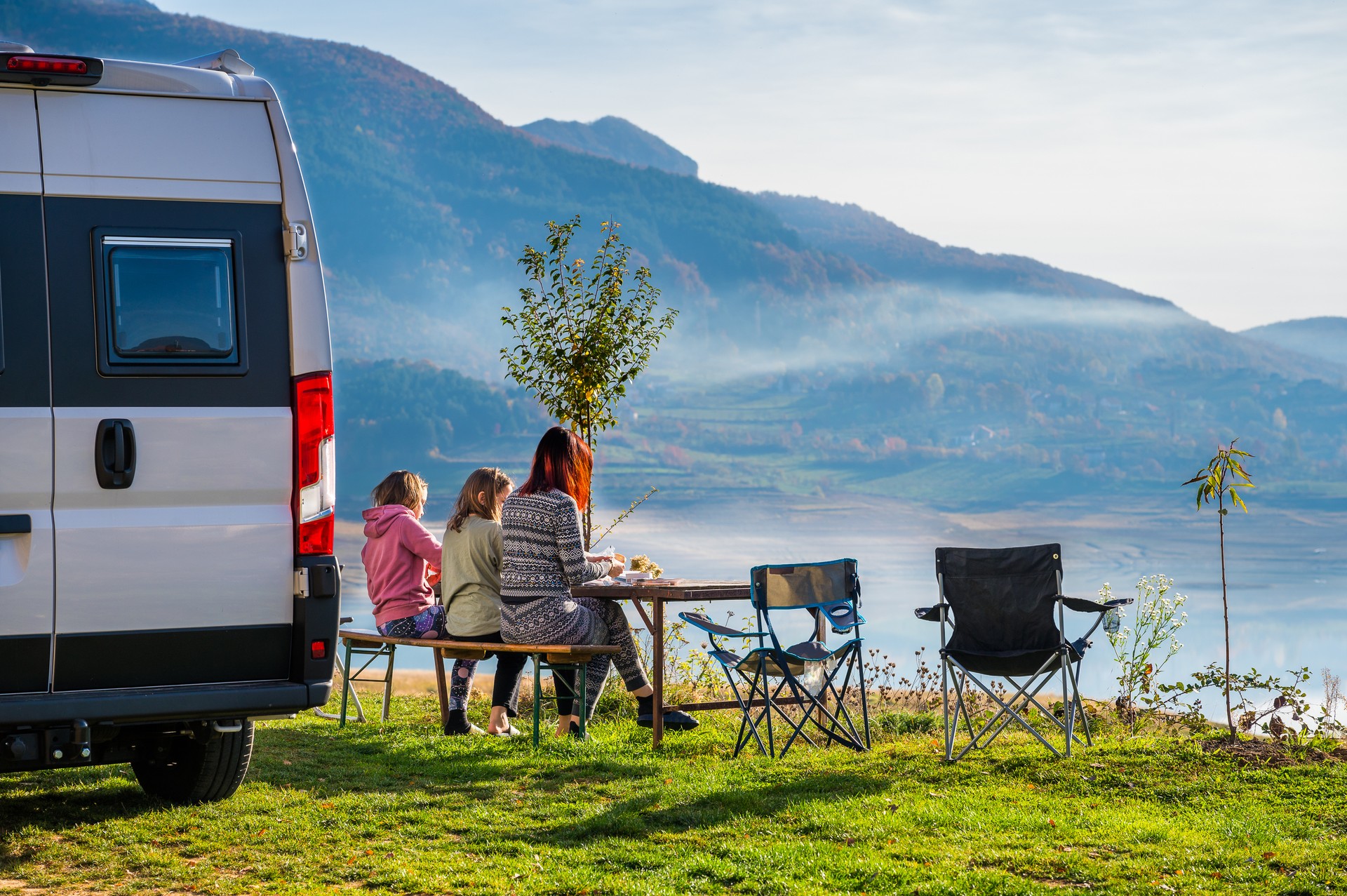 Campervan, Motorhome RV parked next to the lake or river in Bosnia and Herzegovina. Family with camper van or motor home eating breakfast on an active family vacation on a road trip to Ramsko lake.